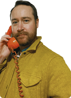 portrait of Ryan wearing a yellow shirt jacket and holding an orange phone to his ear
